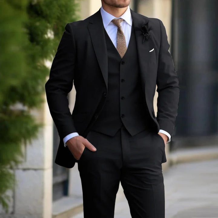 Model wearing the suit in black with matching waistcoat, white shirt and brown tie, hands in pockets 4