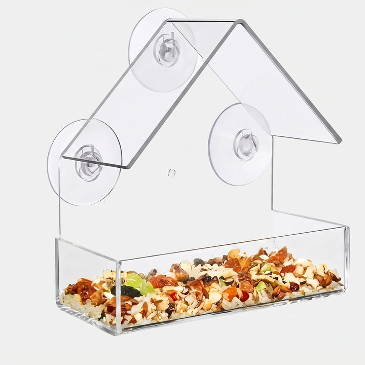 Clear acrylic feeder with a pitched roof, three suction cups and a tray filled with a colourful seed and dried fruit mix. 1