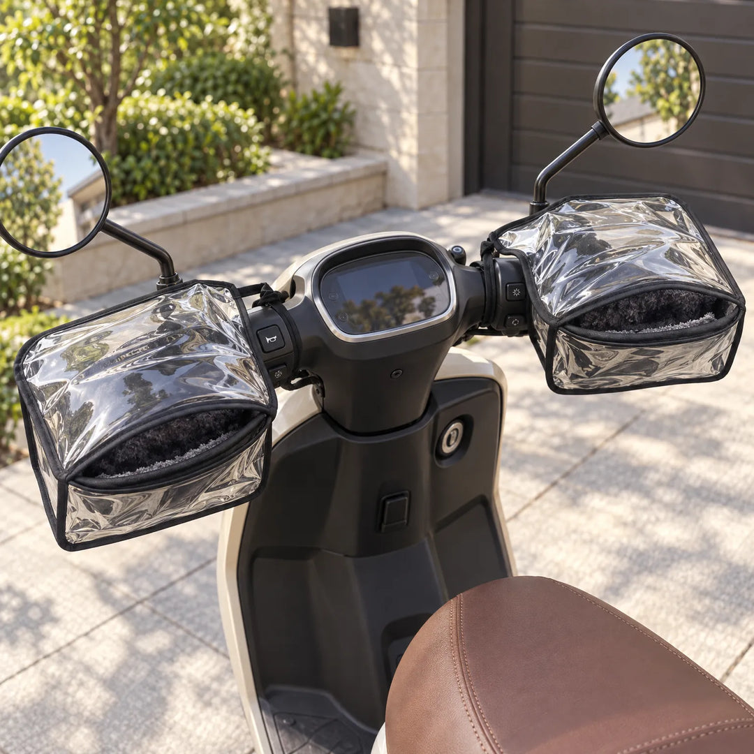 Pair of clear handlebar muffs with black trim and fleece lining fitted on a cream scooter parked in a sunlit driveway. 1
