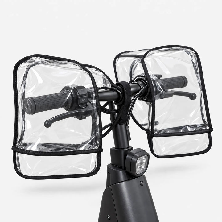 Rear view of clear transparent muffs covering both grips and brake levers of a black scooter handlebar, shown on a white background. 4