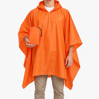 Front view of the orange hooded poncho on a model against white, holding the small matching drawstring pouch it packs into. 2