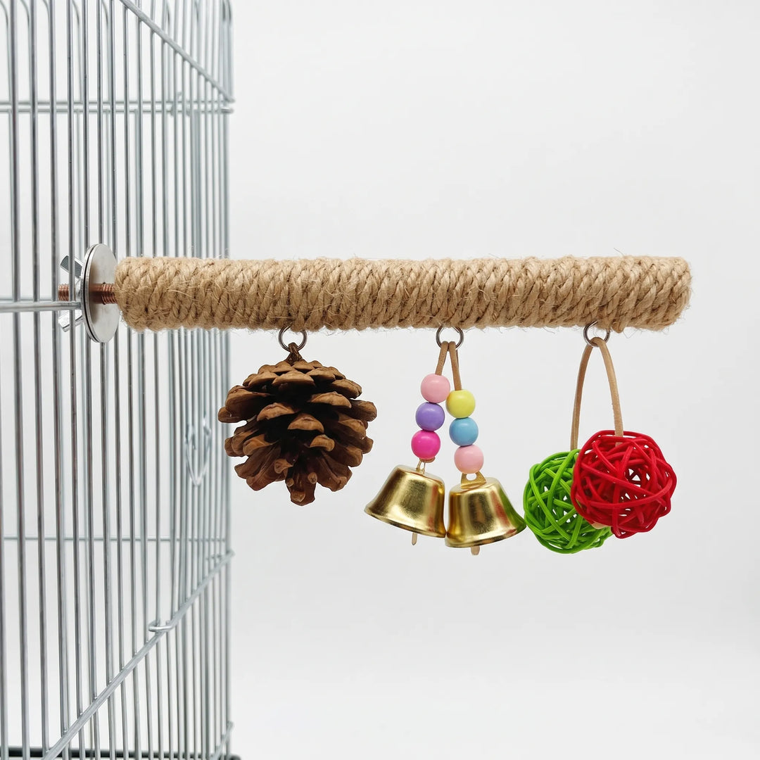 Rope-wrapped bird perch bolted to a wire cage, with a pine cone, two golden bells with beads and two woven balls hanging below. 1