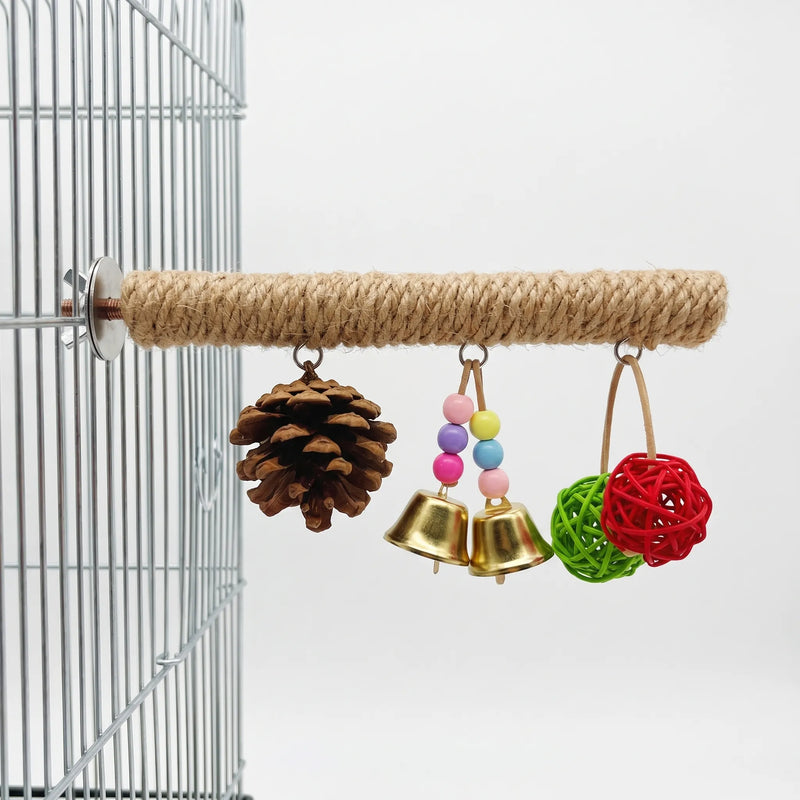 Rope-wrapped bird perch bolted to a wire cage, with a pine cone, two golden bells with beads and two woven balls hanging below. 1