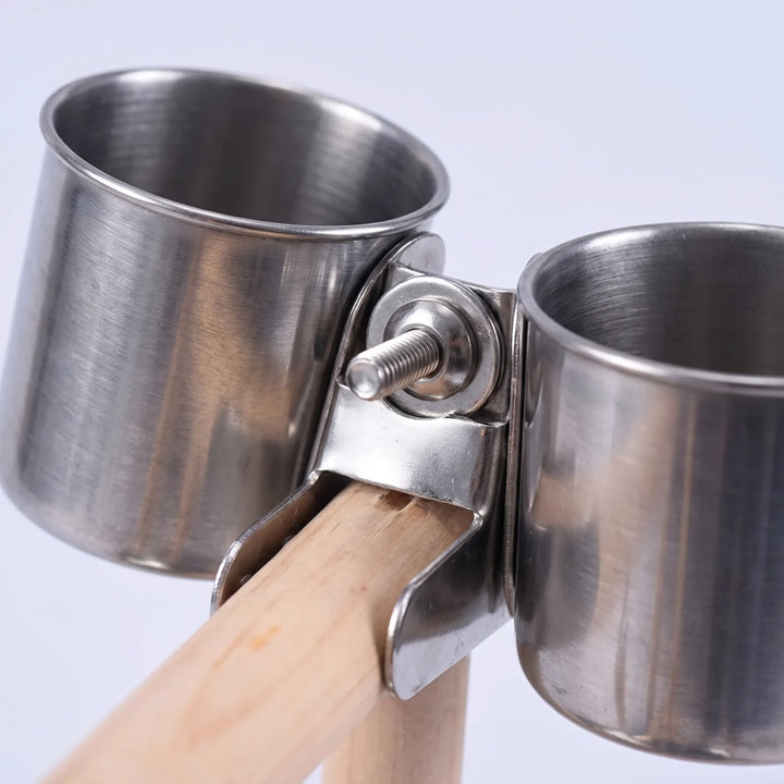Close-up of two stainless steel food cups held by a metal clamp with a screw fixing them to the wooden perch. 4