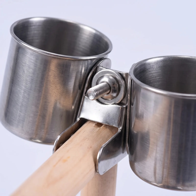 Close-up of two stainless steel food cups held by a metal clamp with a screw fixing them to the wooden perch. 4