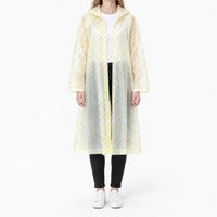 Front view of the translucent raincoat with yellow polka dots, worn open over a white tee and black jeans. 11