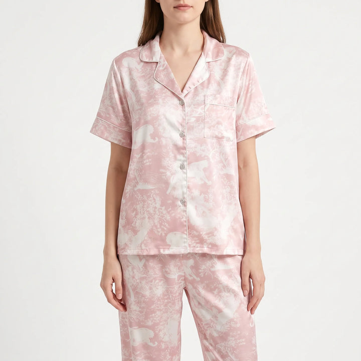 Model wearing a short-sleeve version of the pink and cream printed pyjama shirt with piped edges and pocket, with matching trousers. 6