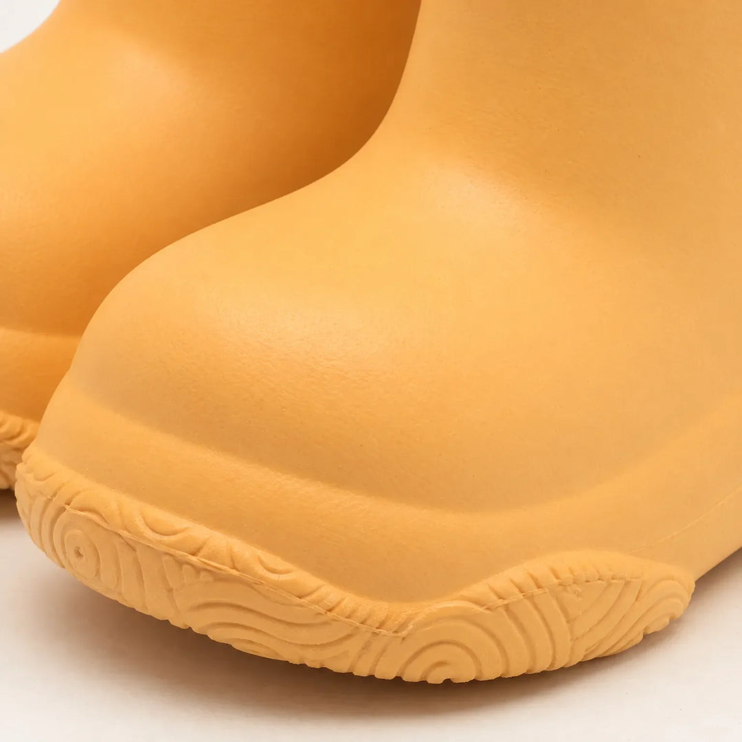 Close-up of the rounded toe and swirl-patterned tread of a yellow-orange welly, showing the smooth moulded surface. 6