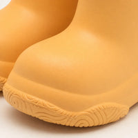 Close-up of the rounded toe and swirl-patterned tread of a yellow-orange welly, showing the smooth moulded surface. 6
