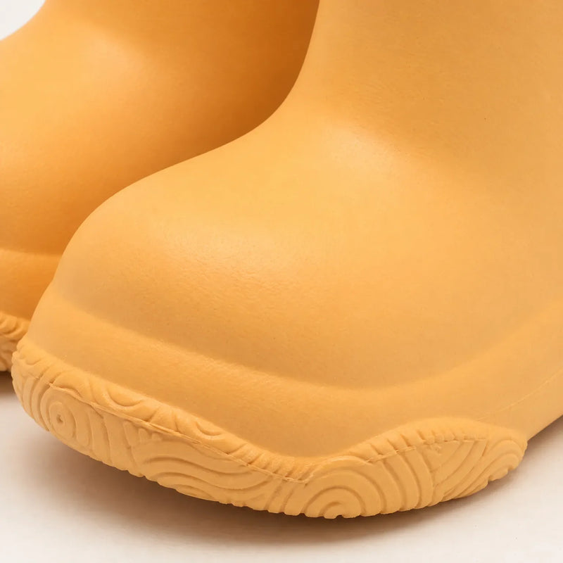 Close-up of the rounded toe and swirl-patterned tread of a yellow-orange welly, showing the smooth moulded surface. 6