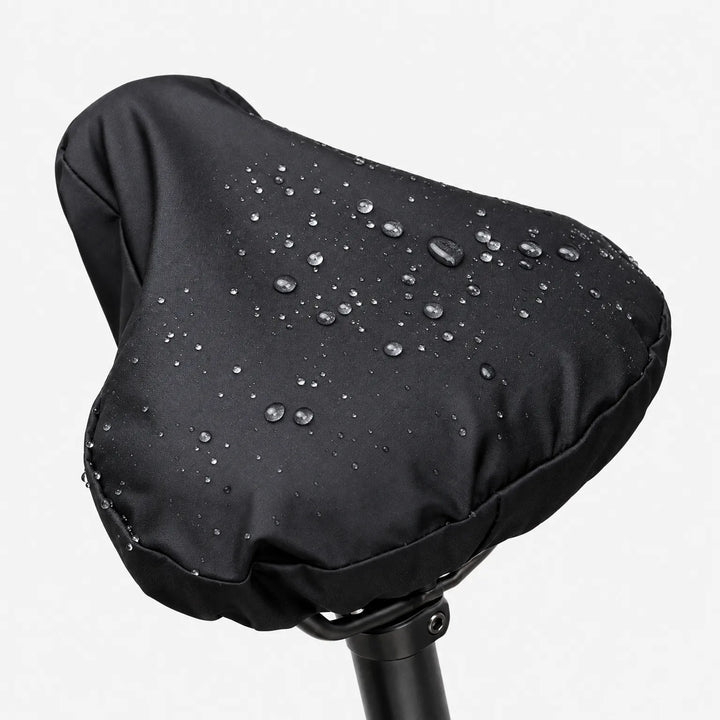 Black saddle cover on a seatpost against a white background, with water droplets beading on the smooth surface. 2