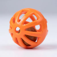 Close-up of a single orange perforated plastic ball with a small brown bead visible inside, on a pale grey background. 4