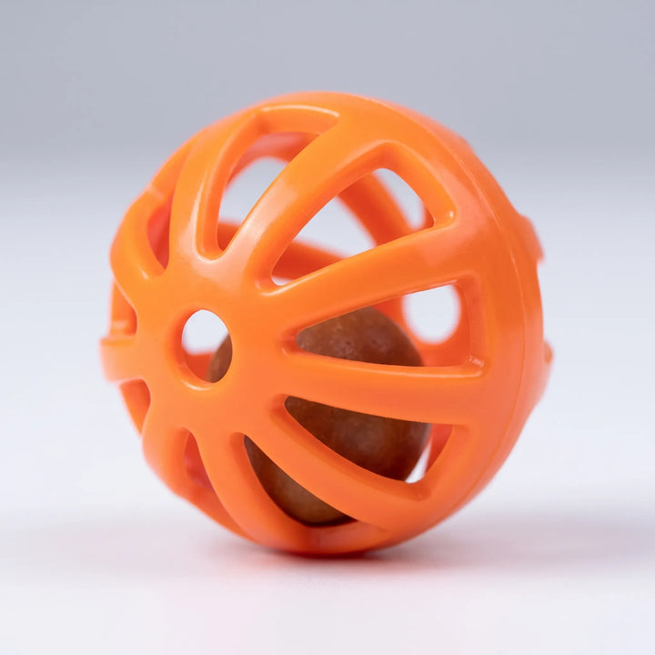 Close-up of a single orange perforated plastic ball with a small brown bead visible inside, on a pale grey background. 4