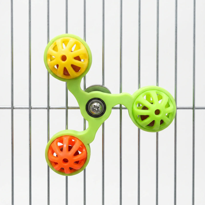 Green spinner with yellow, lime and orange bell balls mounted on the metal bars of a cage, shown against a white background. 5