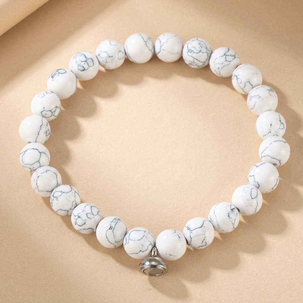 White beaded bracelet with grey marbled veining and a silver magnetic charm, flat on a beige background 3