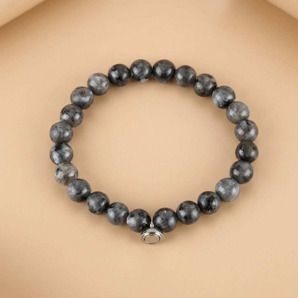 Grey bracelet of dark speckled stone beads with a silver magnetic charm, flat on a warm peach background 4
