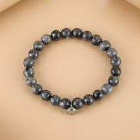 Grey bracelet of dark speckled stone beads with a silver magnetic charm, flat on a warm peach background 4