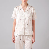 Front view on a model of the short-sleeved buttoned top with chest pocket, lace-trimmed sleeves and scattered bow print. 2