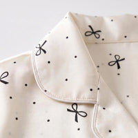 Close-up of the rounded piped collar and button placket, showing the black bow and dot print on cream satin-like fabric. 5