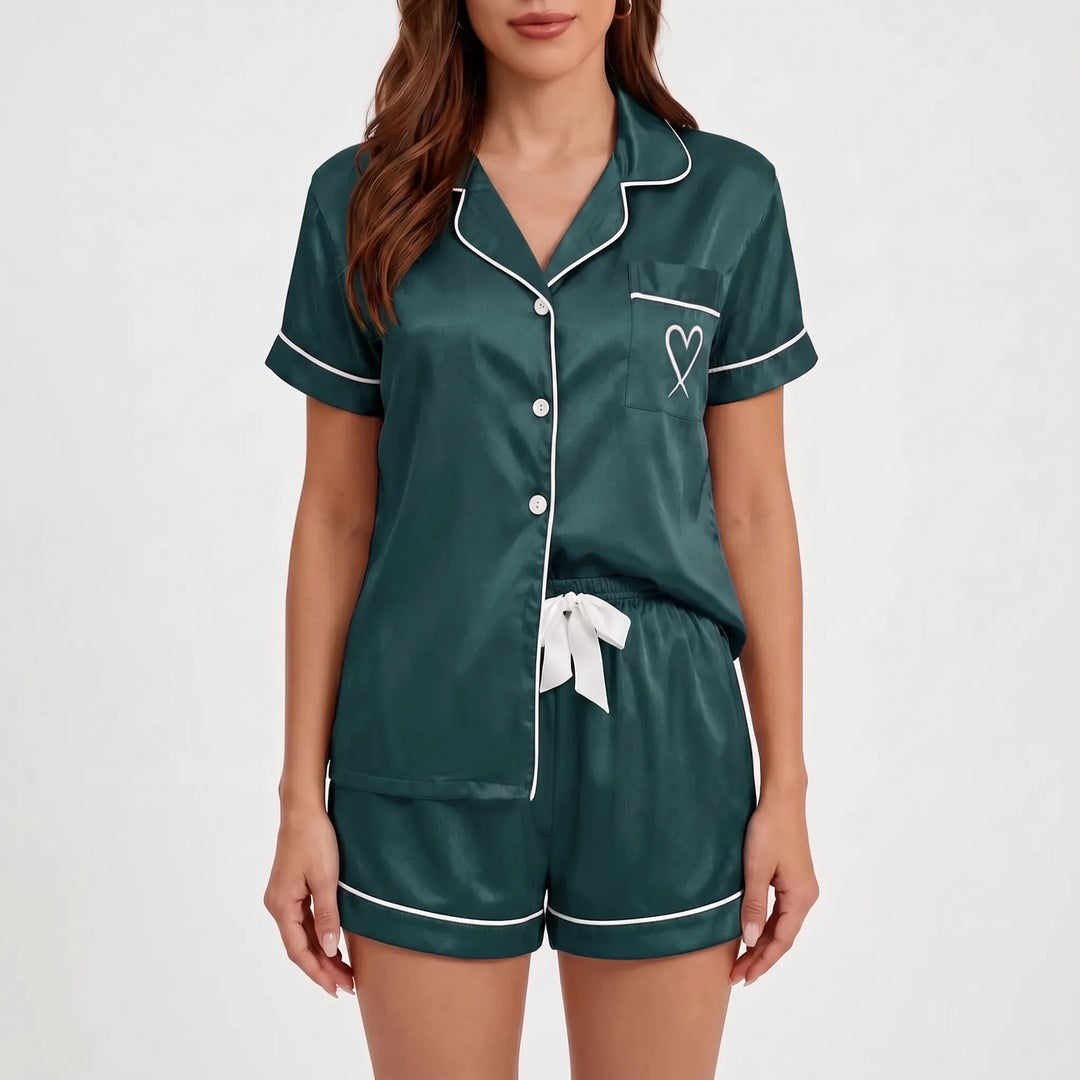 Front view on a plain background of the dark green satin pyjama set with white piping, buttons, heart pocket and white bow. 2