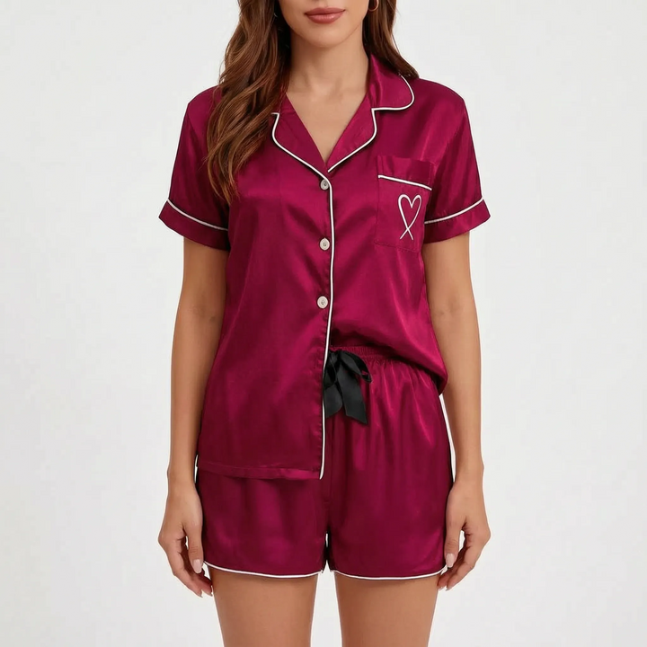 Front view of the burgundy satin pyjama set with white piping, heart pocket and black ribbon bow at the shorts waistband. 7