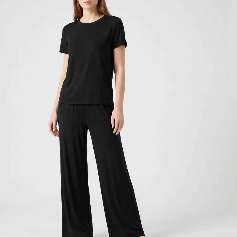 Woman standing in a black short-sleeved crew-neck top and loose wide-leg trousers, front view against a light studio background. 2