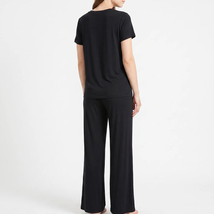 Back view of a model in a black short-sleeved top and long wide-leg trousers, standing barefoot. 3