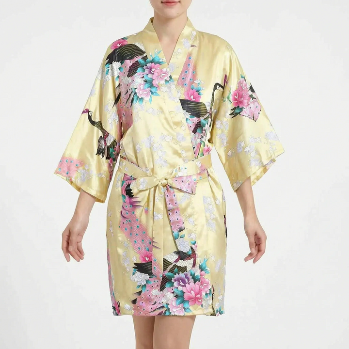 Short satin kimono robe in pale yellow with peacock and pink floral print, worn by a model with the belt tied. 9