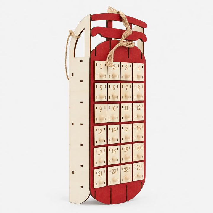 Angled side view of the red sled advent calendar showing the pale plywood side panel, jute loop and rows of numbered drawers. 3