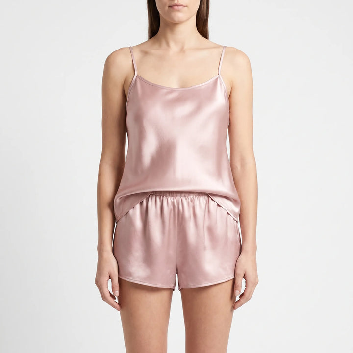 Front view of a model standing in a dusty pink satin camisole with thin straps and elastic-waist shorts. 2