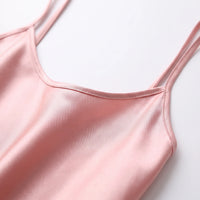 Close-up of the pink satin camisole's scoop neckline, stitched edge and thin double straps lying flat. 5