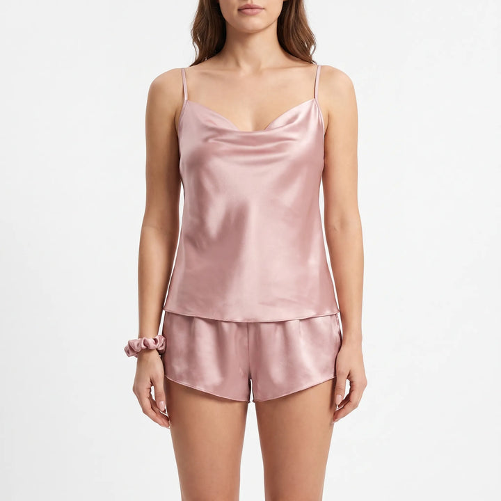 Front view of a model on a white background in the dusty pink satin cowl-neck cami and shorts, with a matching scrunchie on her wrist. 2