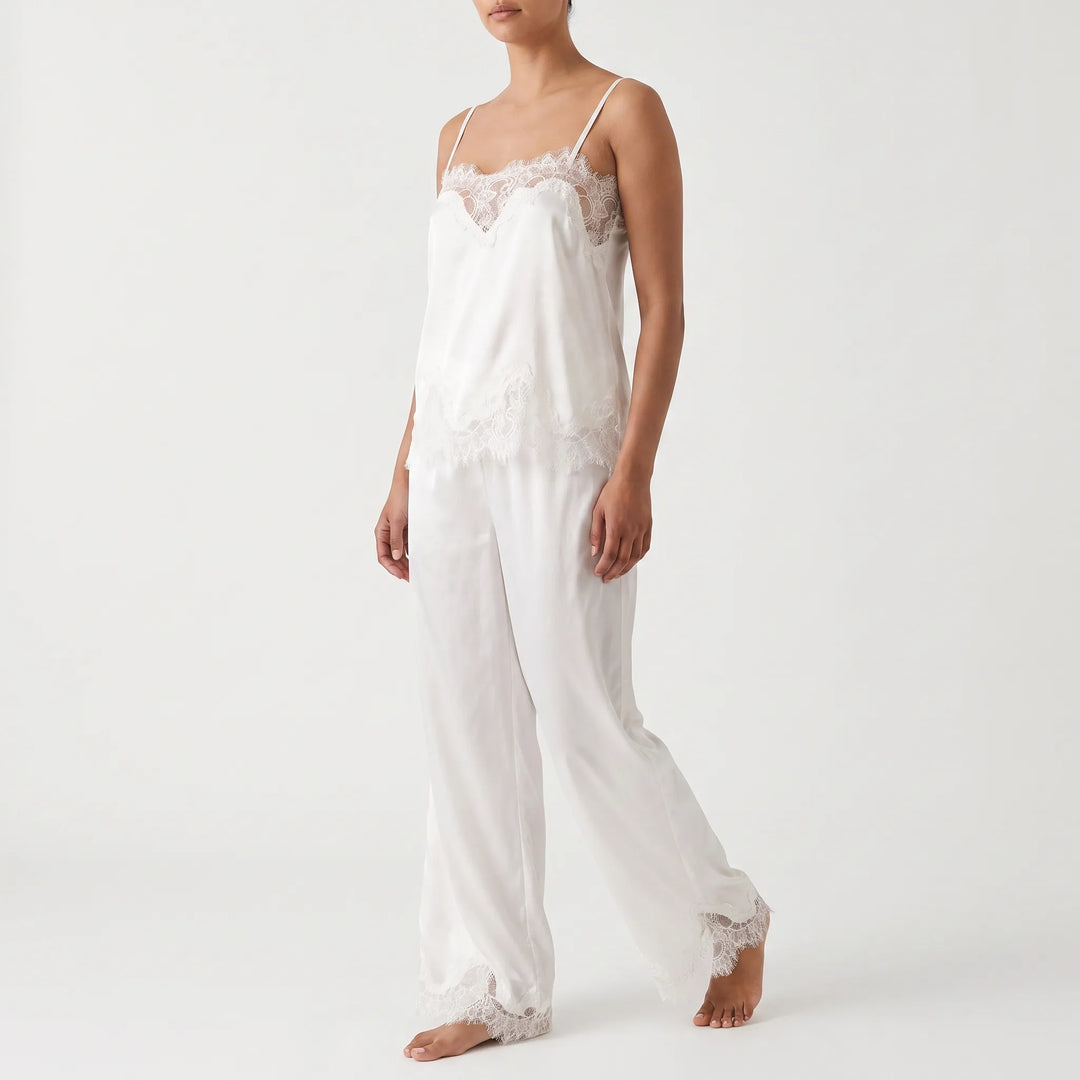Three-quarter front view on a plain studio background of a model walking in the white satin camisole with lace trim and wide-leg trousers. 2