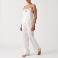 Three-quarter front view on a plain studio background of a model walking in the white satin camisole with lace trim and wide-leg trousers. 2