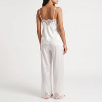 Back view of a model wearing the white satin camisole with scalloped lace edging and thin straps, plus matching wide-leg trousers with lace hems. 3