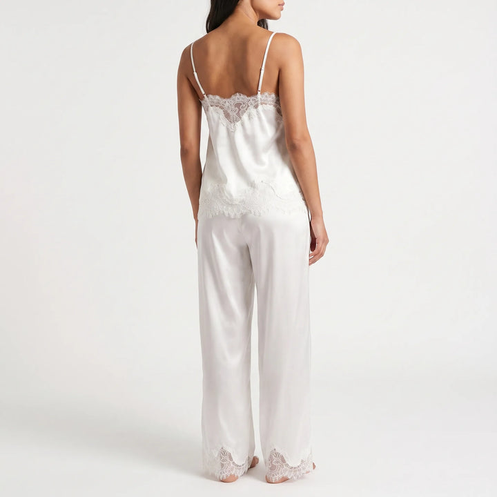 Back view of a model wearing the white satin camisole with scalloped lace edging and thin straps, plus matching wide-leg trousers with lace hems. 3