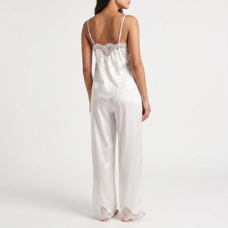Back view of a model wearing the white satin camisole with scalloped lace edging and thin straps, plus matching wide-leg trousers with lace hems. 3
