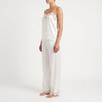 Side view of a model in the white satin set, showing the lace-trimmed camisole neckline and hem and the lace-edged trouser cuffs. 4