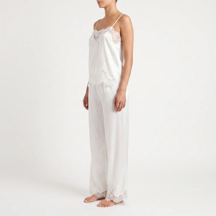 Side view of a model in the white satin set, showing the lace-trimmed camisole neckline and hem and the lace-edged trouser cuffs. 4