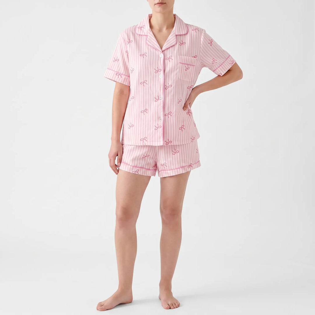 Model with hand on hip wearing the short-sleeved pink striped bow-print pyjama shirt with the matching shorts, shown from the front. 2