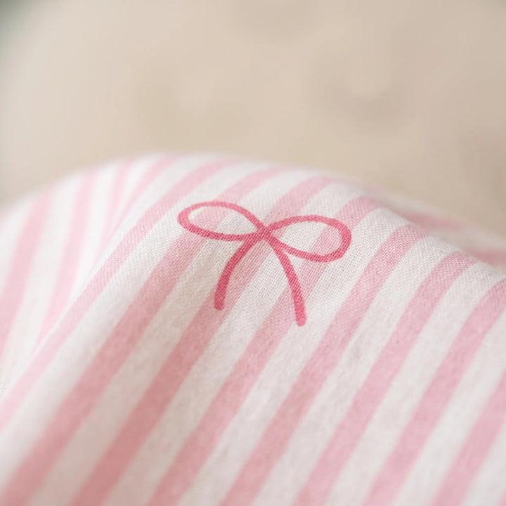 Close-up of the woven fabric showing a single hand-drawn pink bow printed over soft pink and white stripes. 6