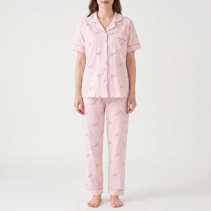 Model facing forward on a plain background wearing the pink striped bow-print shirt with contrast piping and matching long trousers. 7