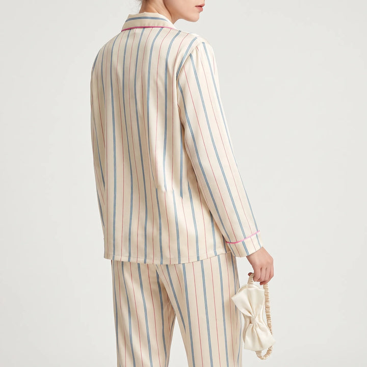 Back view of the striped pyjama top and trousers on a model, holding the bow-trimmed eye mask by its elastic strap. 3