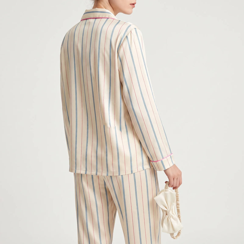 Back view of the striped pyjama top and trousers on a model, holding the bow-trimmed eye mask by its elastic strap. 3