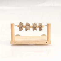 Front view of a wooden perch platform with two upright posts, a bar strung with wooden beads and bark slices, and metal discs behind. 1