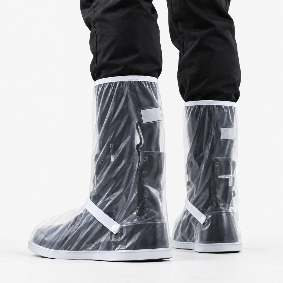 Rear three-quarter view of clear shoe covers with white trim, strap and snap button, worn over black boots against white background. 4