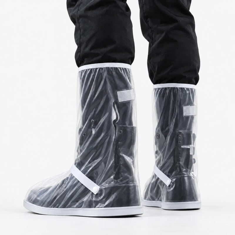 Rear three-quarter view of clear shoe covers with white trim, strap and snap button, worn over black boots against white background. 4