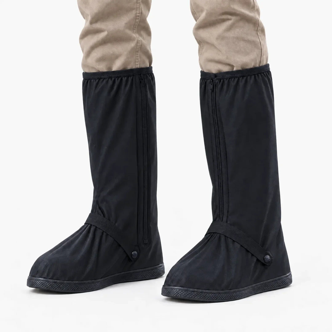 Front view of black tall shoe covers with front zippers and ankle straps worn over khaki trousers on a white background. 7