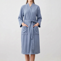 Front view of a model in the blue robe with both hands in the patch pockets and the belt tied in a bow. 6