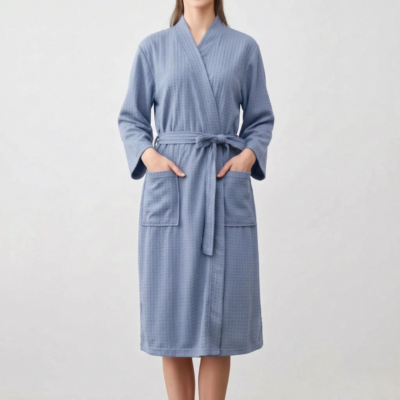 Front view of a model in the blue robe with both hands in the patch pockets and the belt tied in a bow. 6